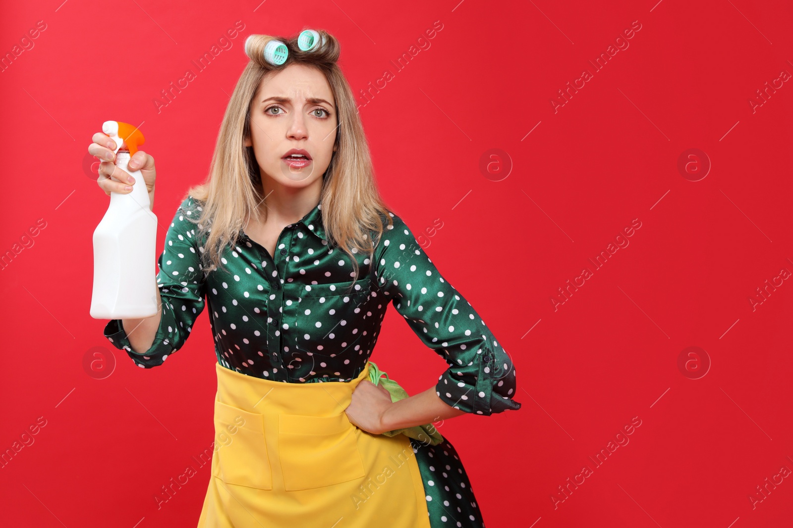 Photo of Young housewife with detergent and rag on red background. Space for text