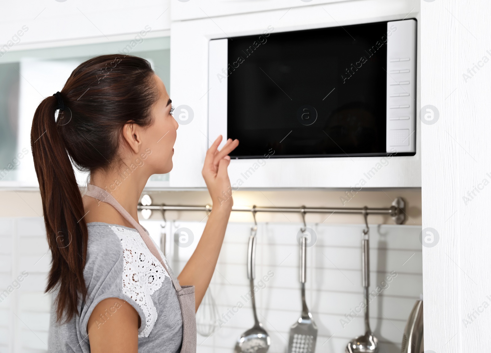 Photo of Young woman using microwave oven at home