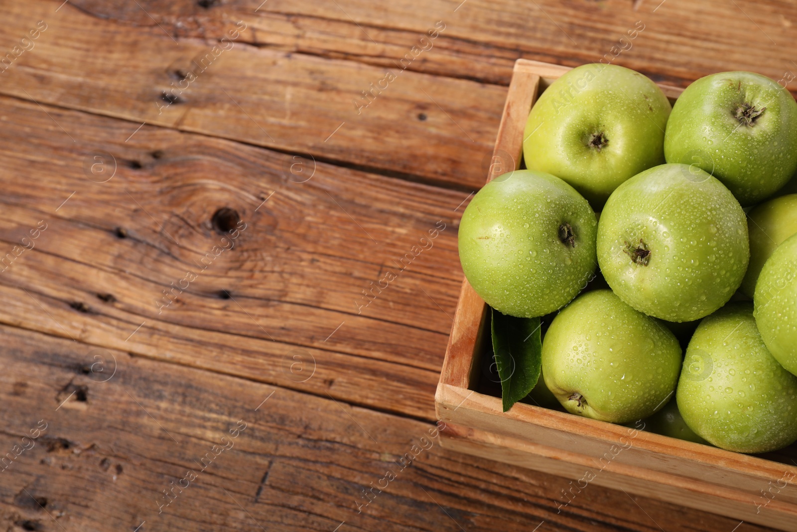 Photo of Fresh ripe green apples with water drops in crate on wooden table. Space for text