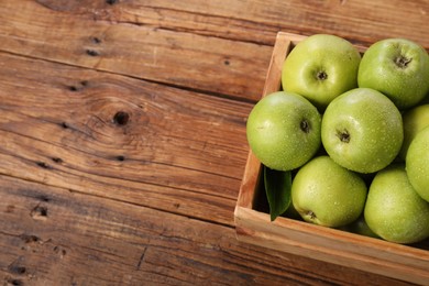 Photo of Fresh ripe green apples with water drops in crate on wooden table. Space for text