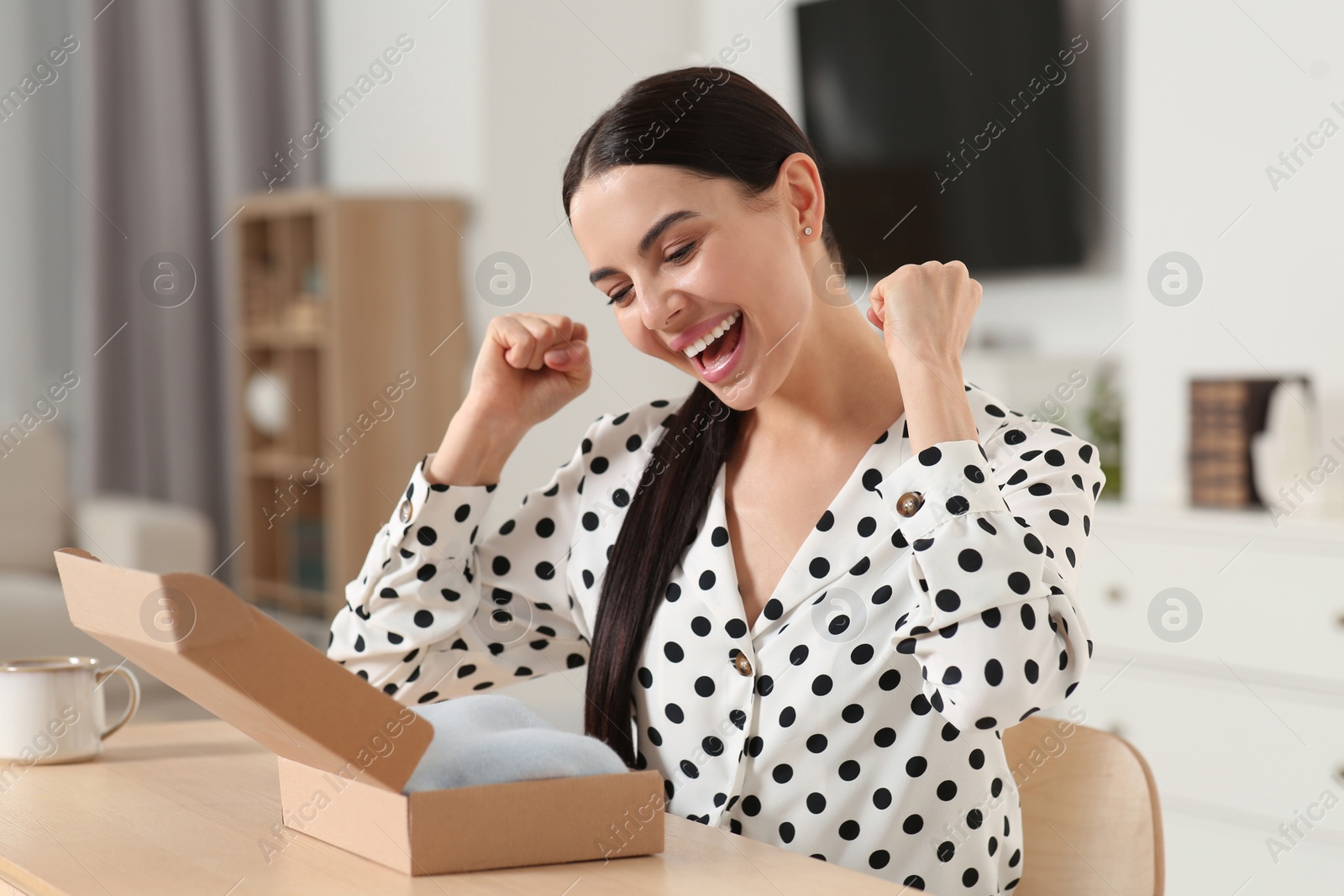 Photo of Emotional young woman with parcel at table indoors. Internet shopping