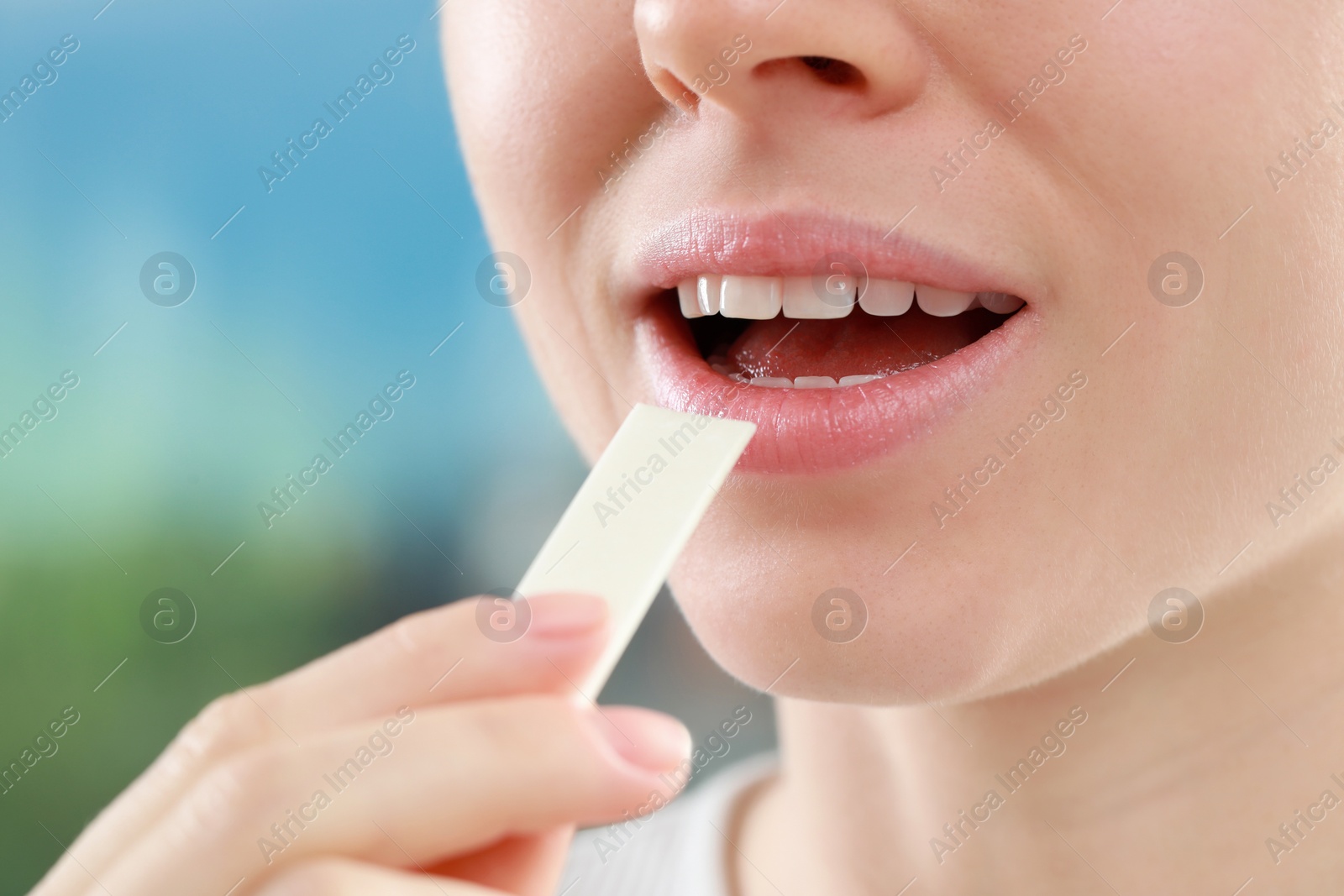 Photo of Woman putting chewing gum piece into mouth on blurred background, closeup