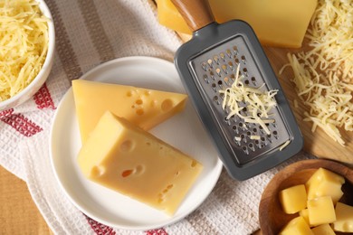 Grated, cut cheese and grater on wooden table, flat lay