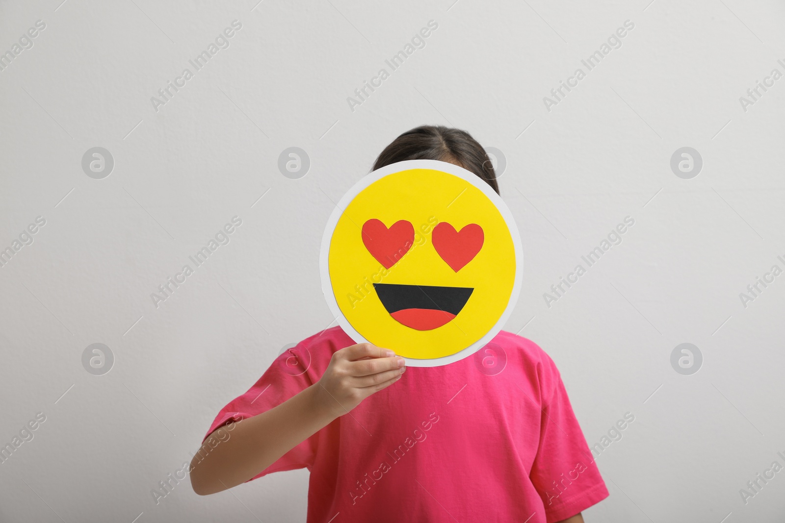 Photo of Little girl covering face with heart eyes emoji on white background