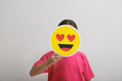 Photo of Little girl covering face with heart eyes emoji on white background