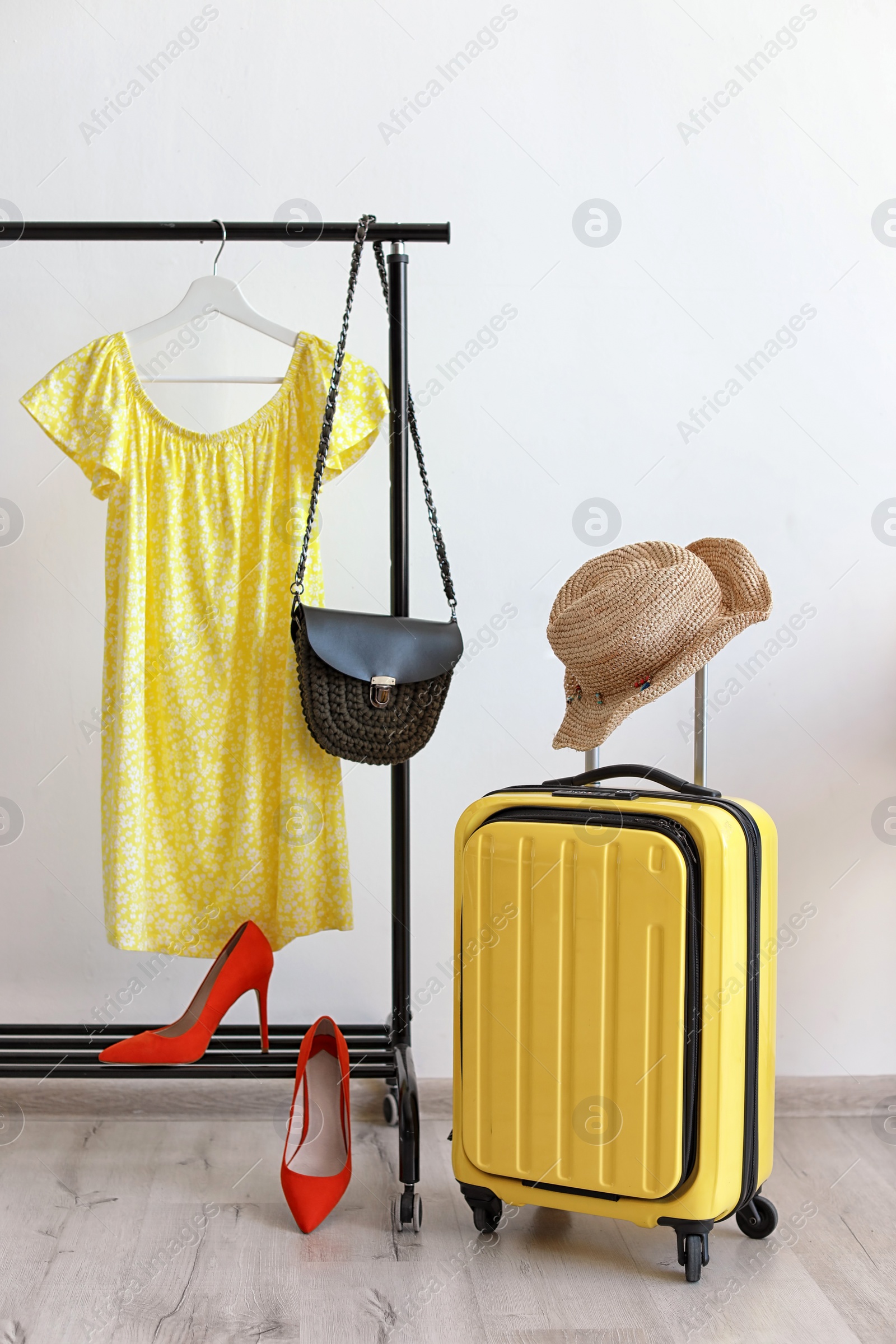 Photo of Packed yellow suitcase and rack with clothes indoors