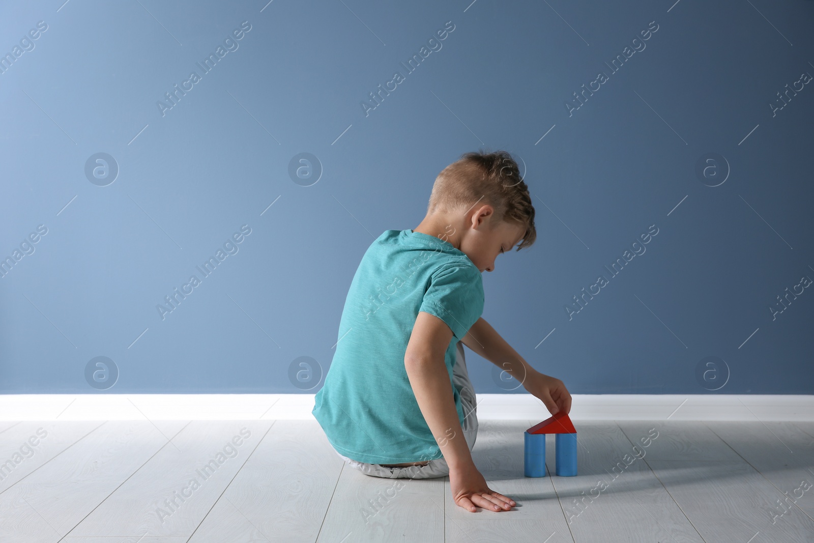 Photo of Little boy with toy sitting on floor near color wall in empty room. Autism concept