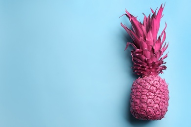 Photo of Top view of painted pink pineapple on light blue background, space for text. Creative concept
