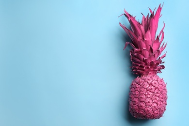 Top view of painted pink pineapple on light blue background, space for text. Creative concept