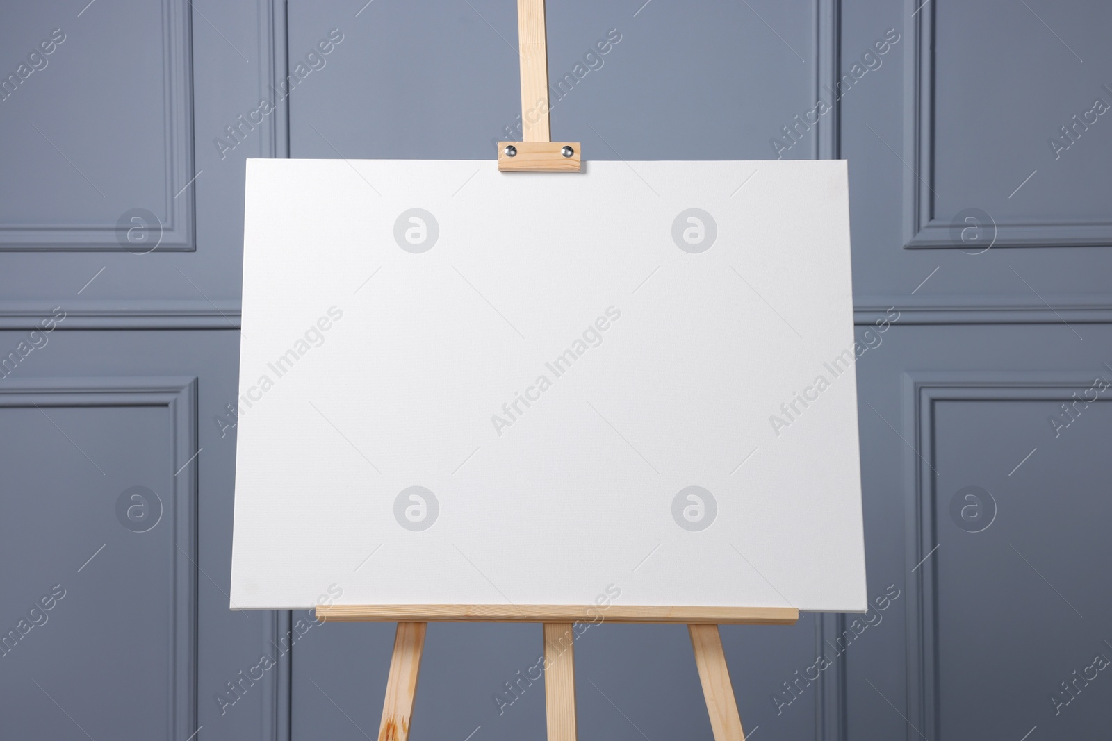 Photo of Wooden easel with blank canvas near grey wall indoors, closeup. Space for text