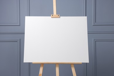 Wooden easel with blank canvas near grey wall indoors, closeup. Space for text