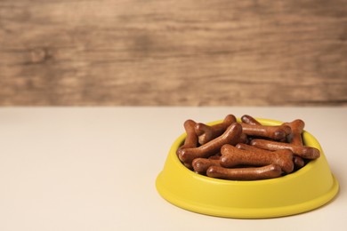 Yellow bowl with bone shaped dog cookies on light table, space for text