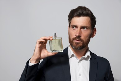 Photo of Handsome bearded man with bottleperfume on light grey background. Space for text