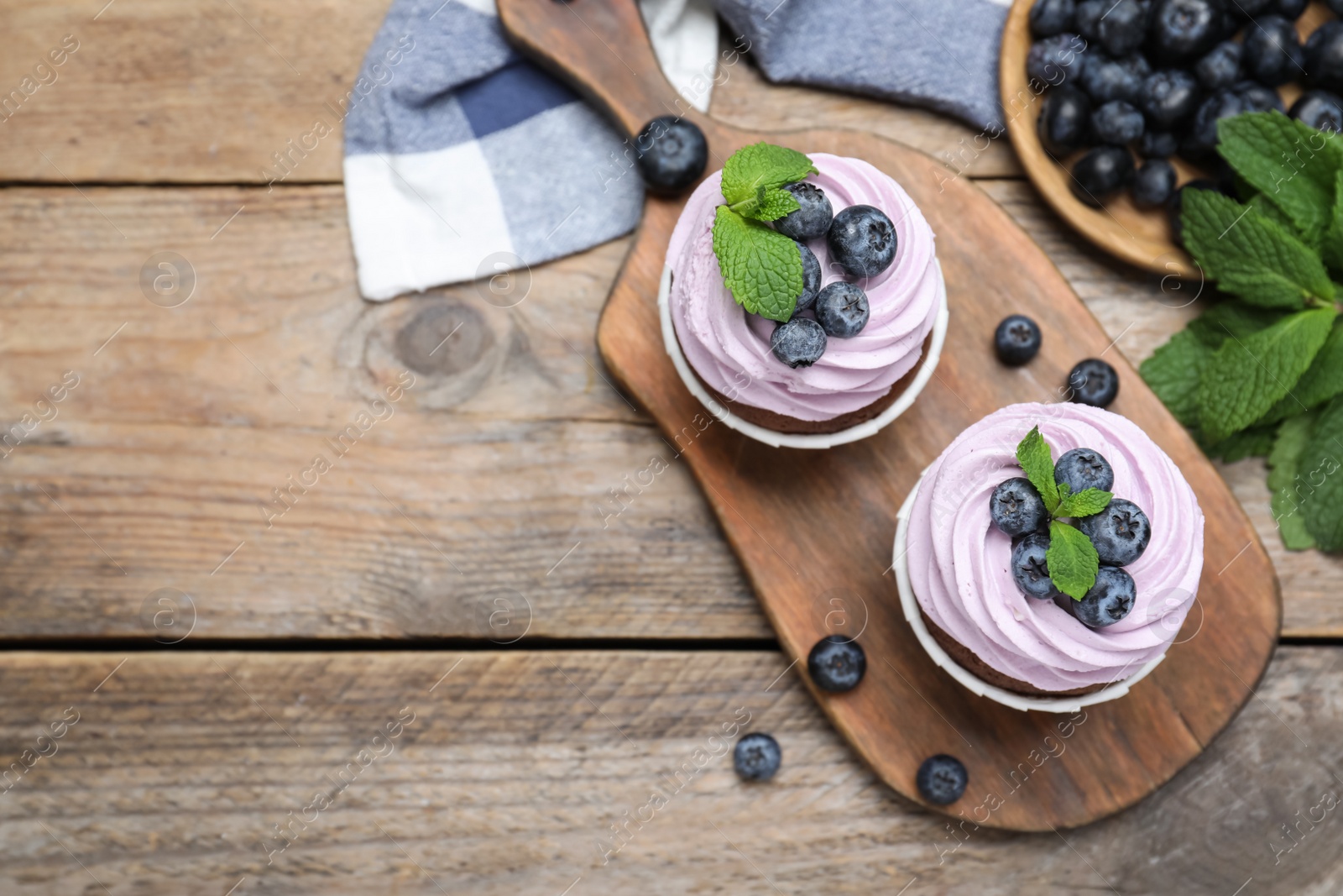 Photo of Sweet cupcakes with fresh blueberries on wooden table, flat lay. Space for text