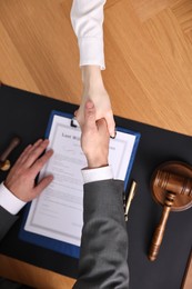 Notary shaking hands with client at wooden table, top view