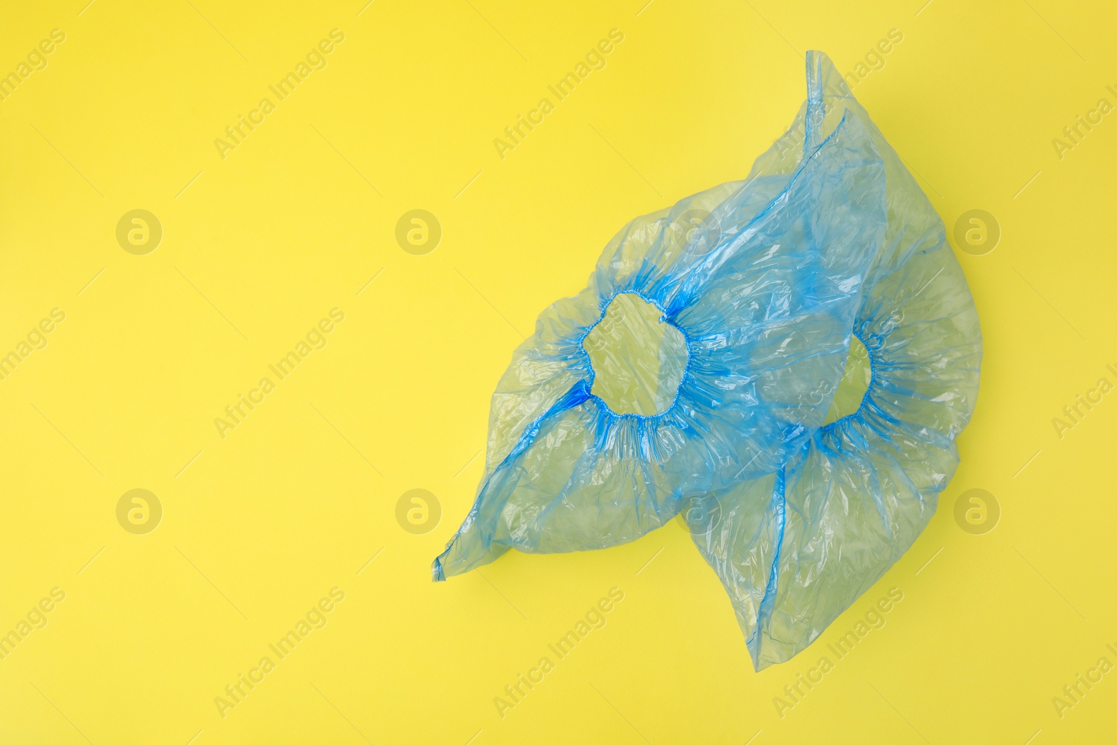 Photo of Pair of blue medical shoe covers on yellow background, top view. Space for text