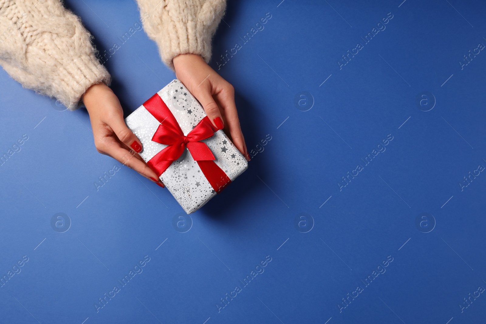 Photo of Christmas present. Woman with gift box on blue background, top view. Space for text