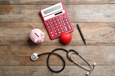 Photo of Flat lay composition with calculator and stethoscope on wooden background. Health insurance concept