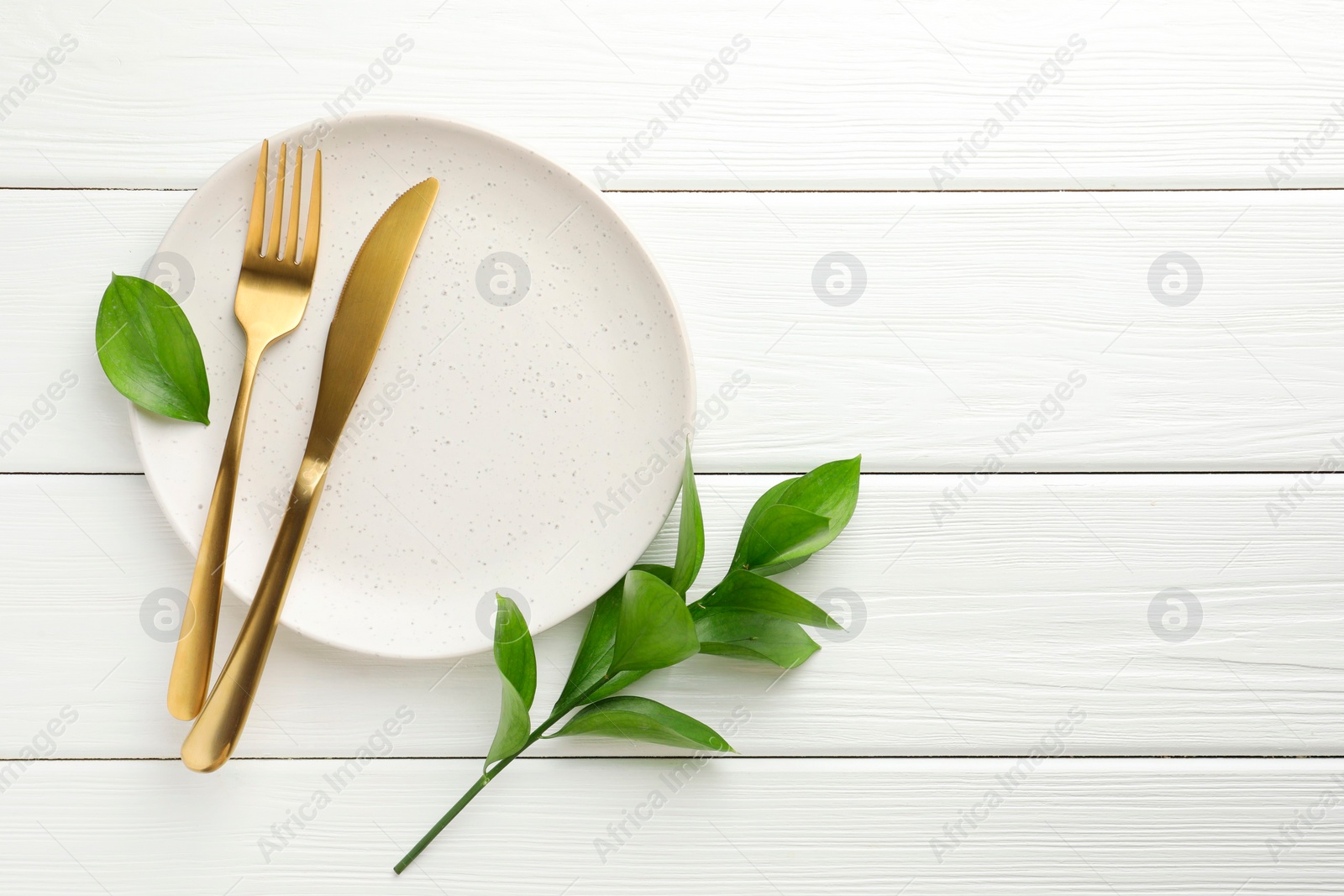 Photo of Stylish setting with cutlery, green leaves and plate on white wooden table, flat lay. Space for text