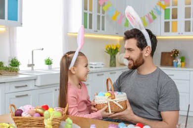 Photo of Father and his cute daughter with wicker basket full of Easter eggs in kitchen