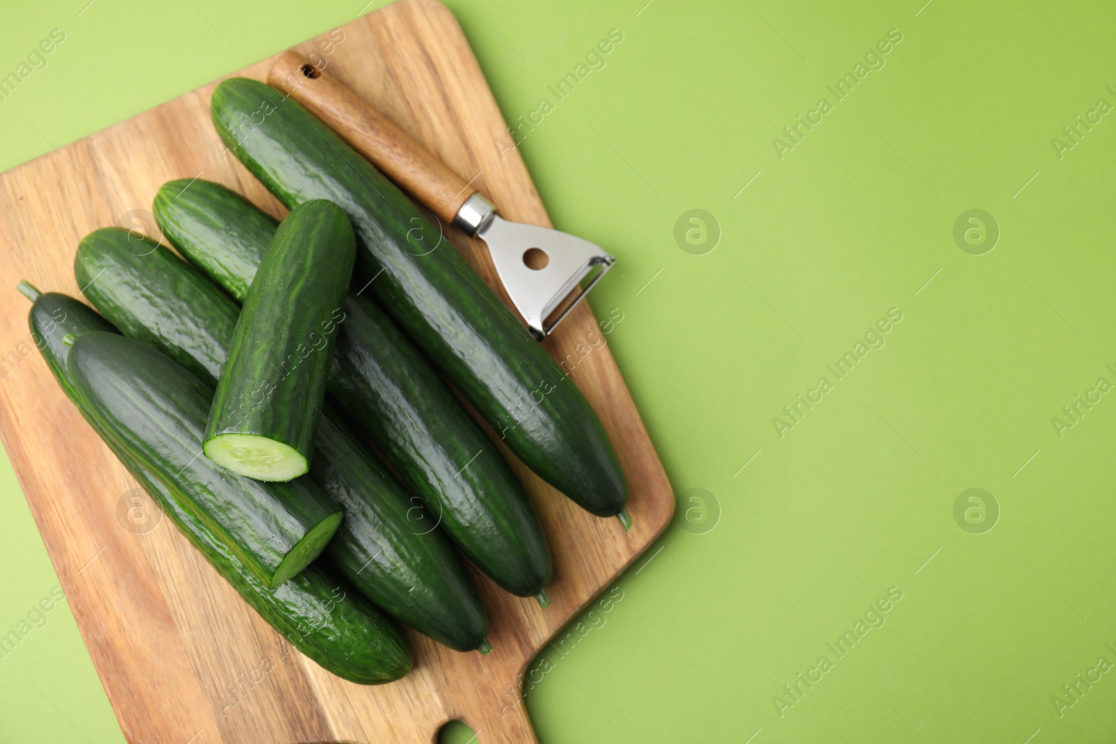 Photo of Fresh cucumbers and peeler on green background, top view. Space for text