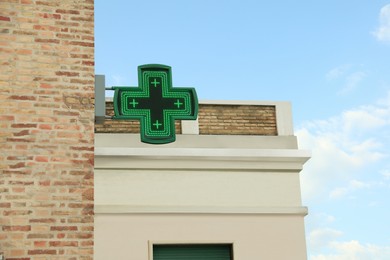 Green cross sign of drugstore on building wall against blue sky