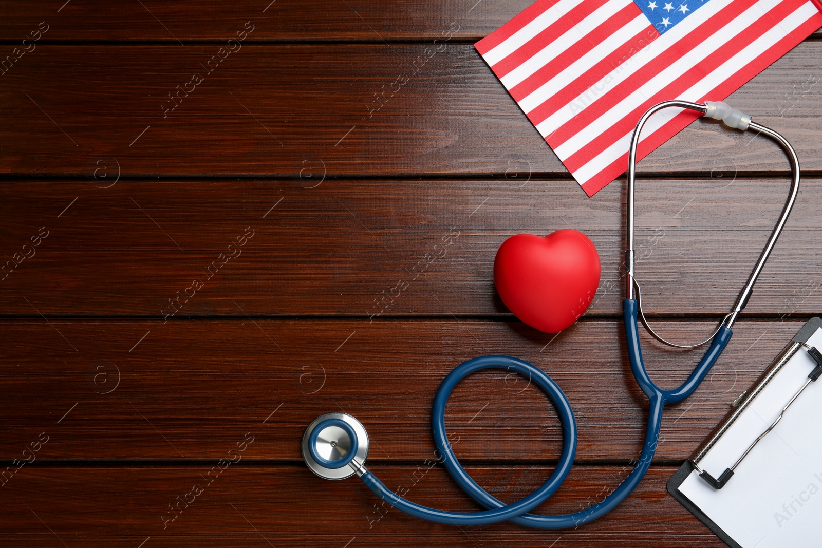 Photo of Stethoscope, red heart, clipboard and American flag on wooden table, flat lay. Space for text