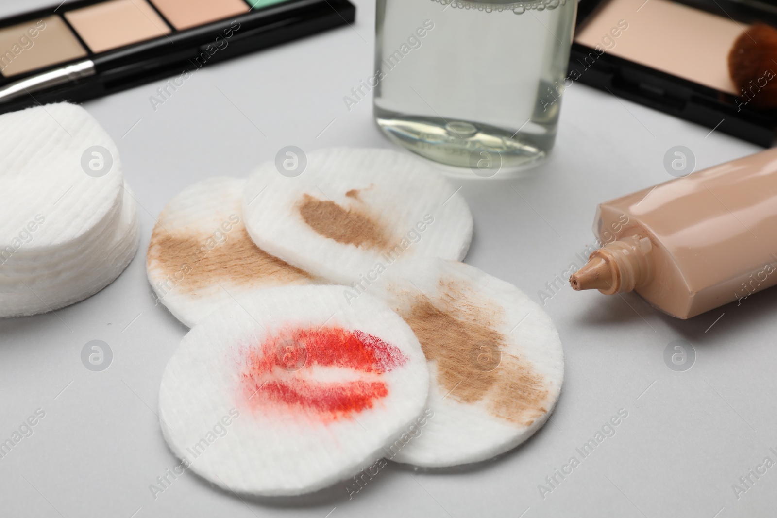 Photo of Dirty cotton pads after removing makeup and different cosmetic products on light grey background, closeup