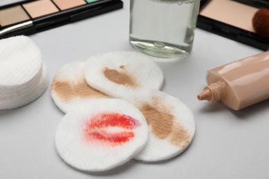 Dirty cotton pads after removing makeup and different cosmetic products on light grey background, closeup