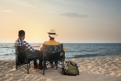 Couple sitting in camping chairs and enjoying seascape on beach, back view