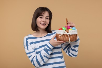 Photo of Easter celebration. Happy woman with wicker basket full of painted eggs on beige background