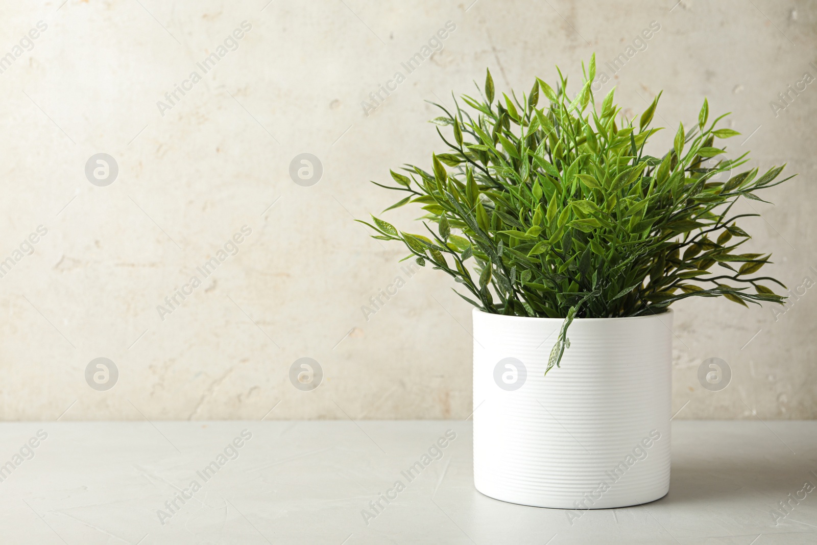 Photo of Artificial plant in white flower pot on table against light background. Space for text