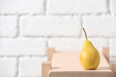 Ripe pear on wooden shelf against blurred background. Space for text