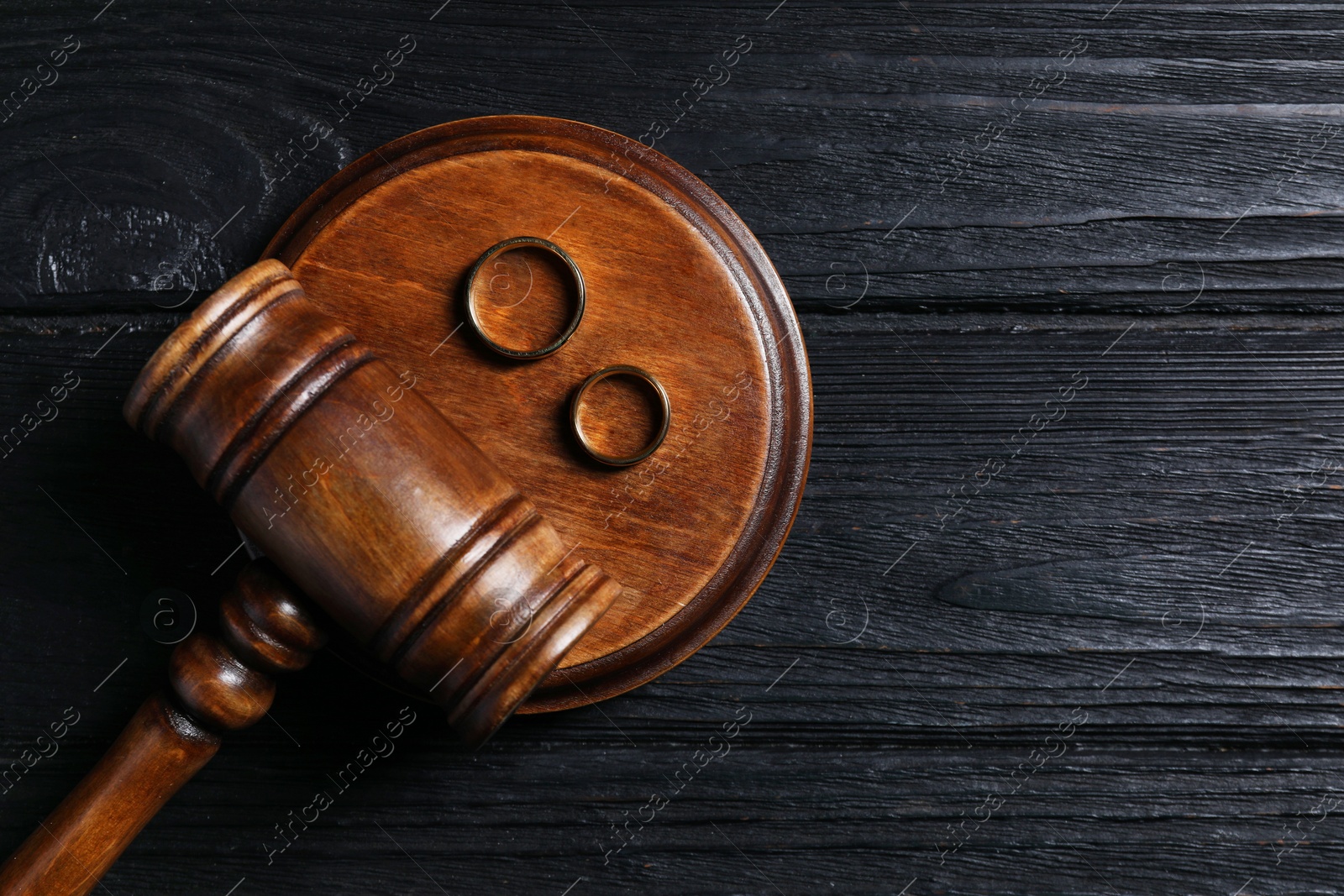 Photo of Divorce concept. Gavel and wedding rings on black wooden table, top view with space for text