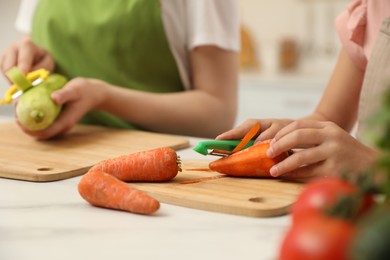 Photo of Mother and daughter peeling vegetables at table in kitchen, closeup