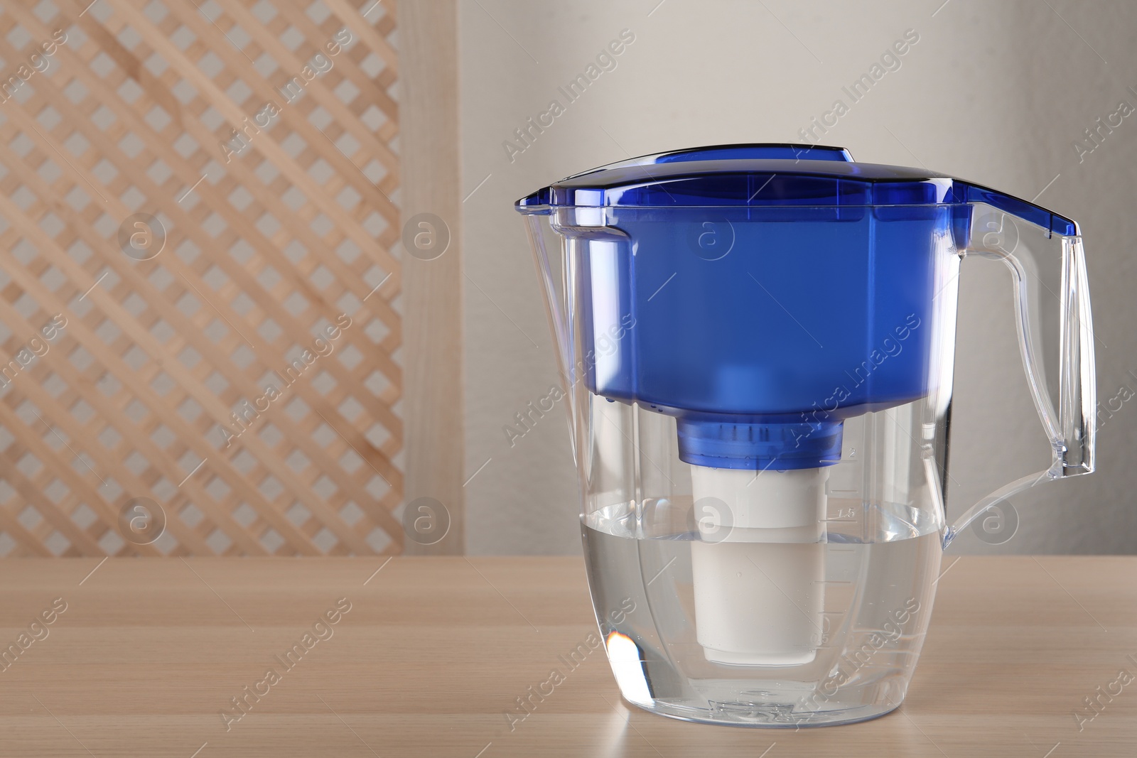 Photo of Filter jug with purified water on wooden table indoors. Space for text