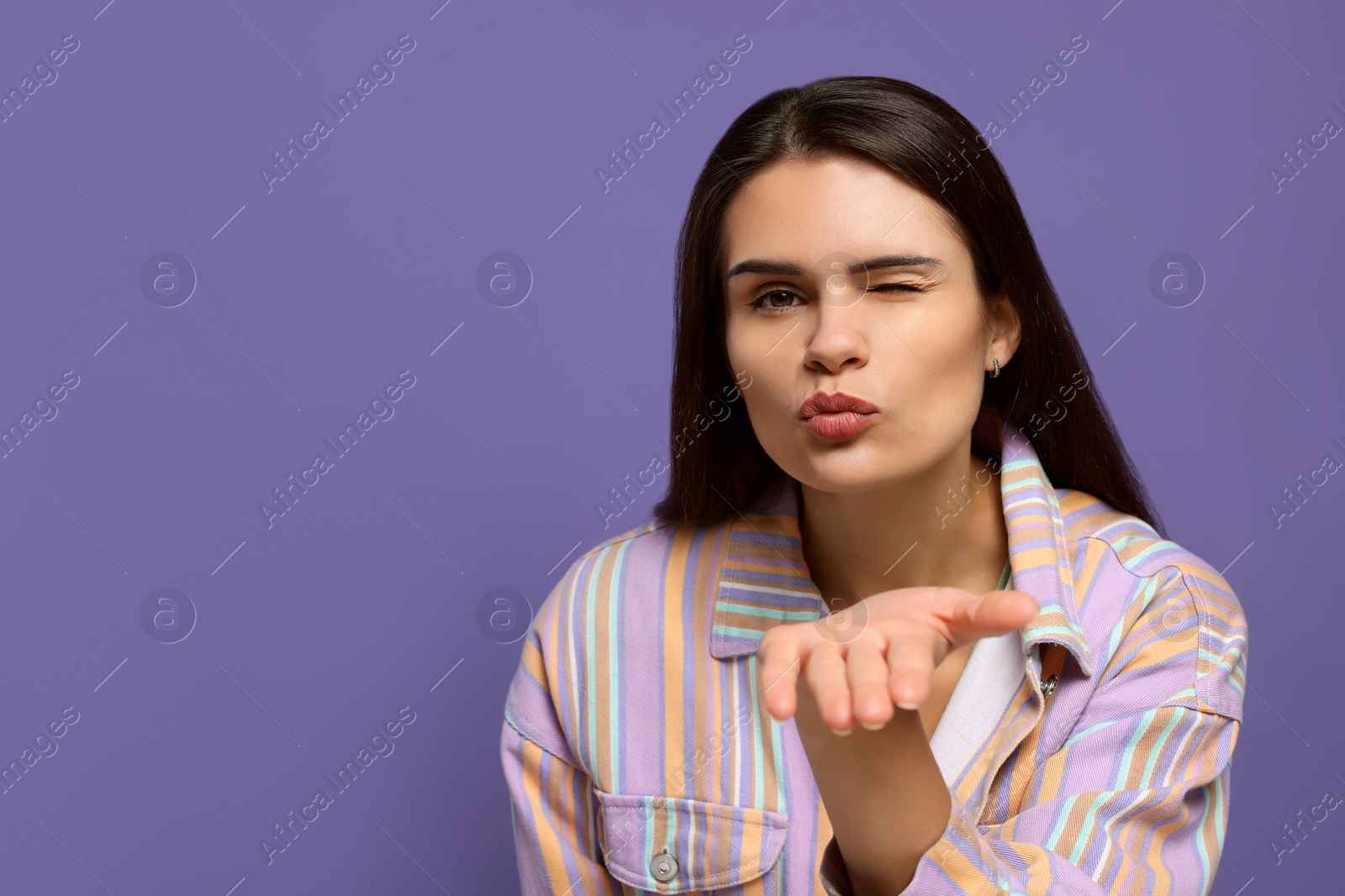 Photo of Beautiful young woman blowing kiss on purple background. Space for text