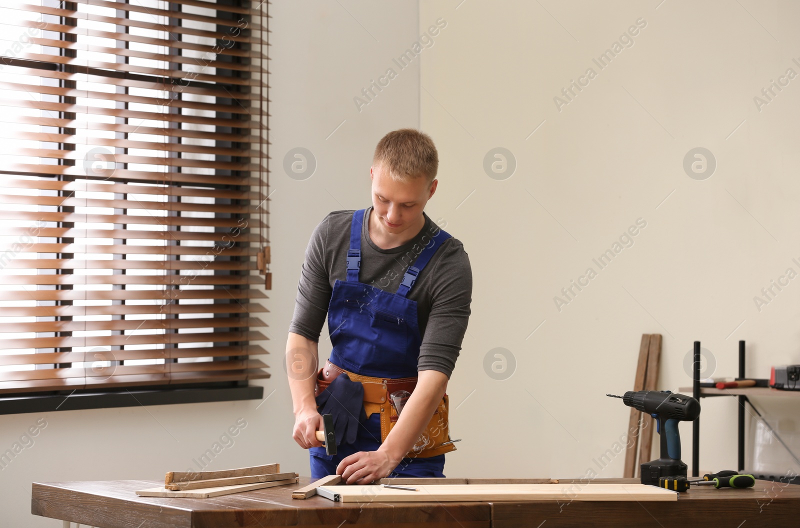 Photo of Handsome young working man using hammer indoors. Home repair