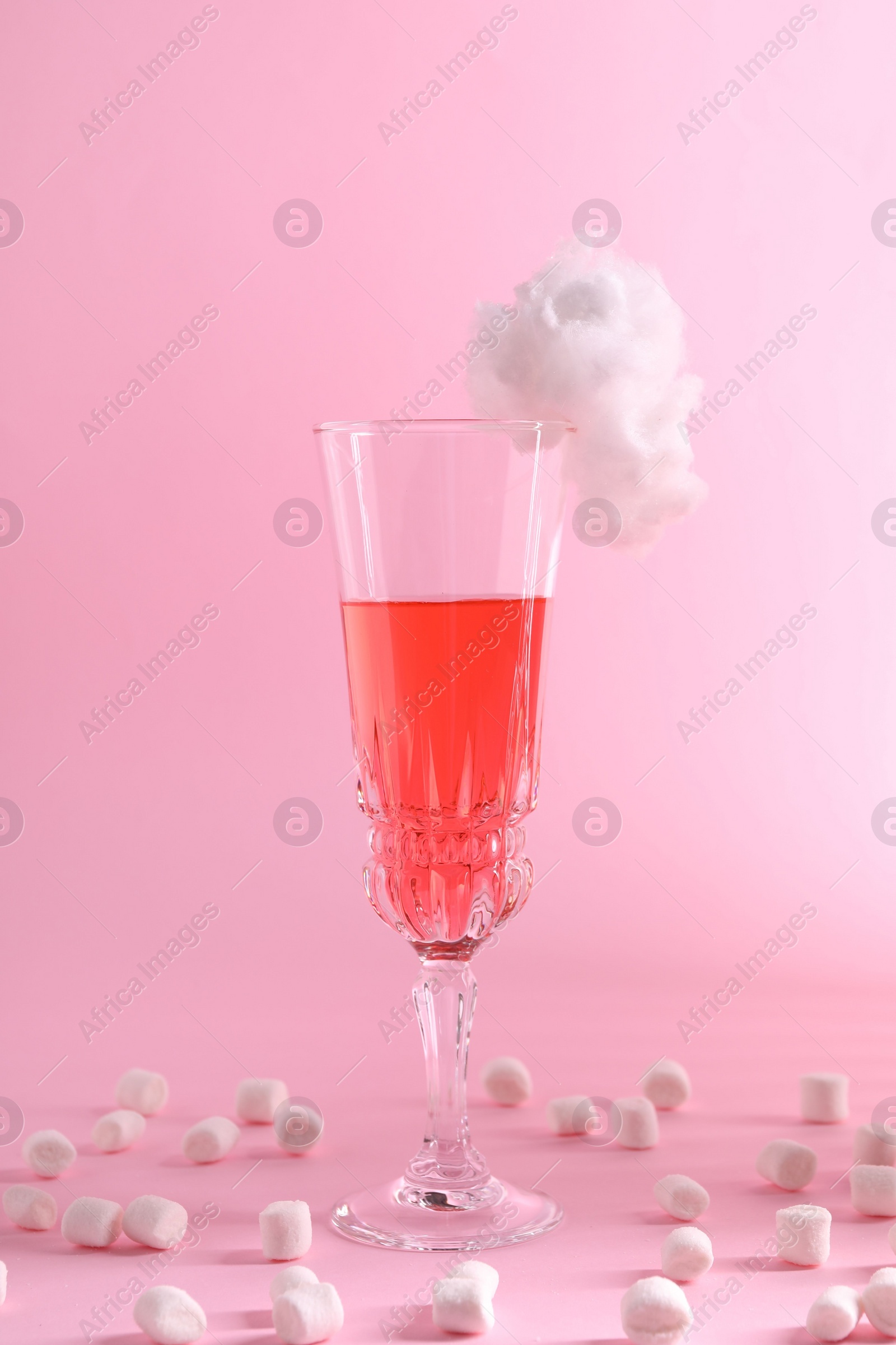 Photo of Tasty cocktail in glass decorated with cotton candy and marshmallows on pink background