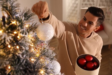 Handsome man decorating Christmas tree at home, above view