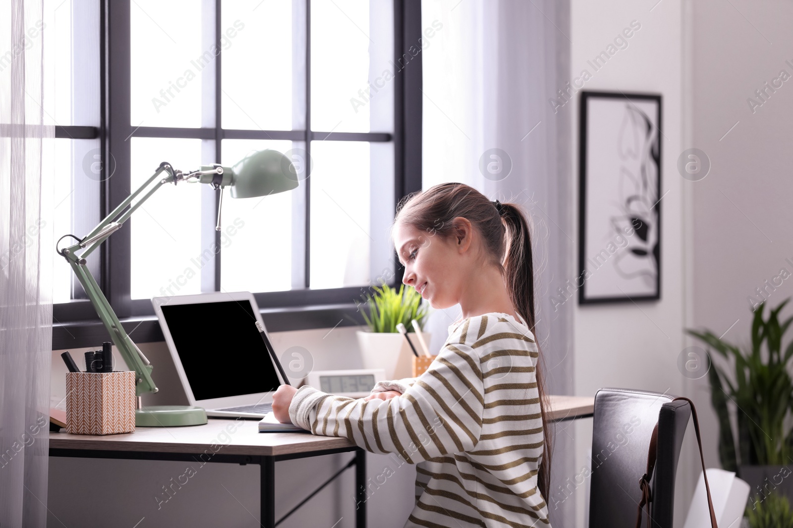 Photo of Pretty preteen girl doing homework at table in room