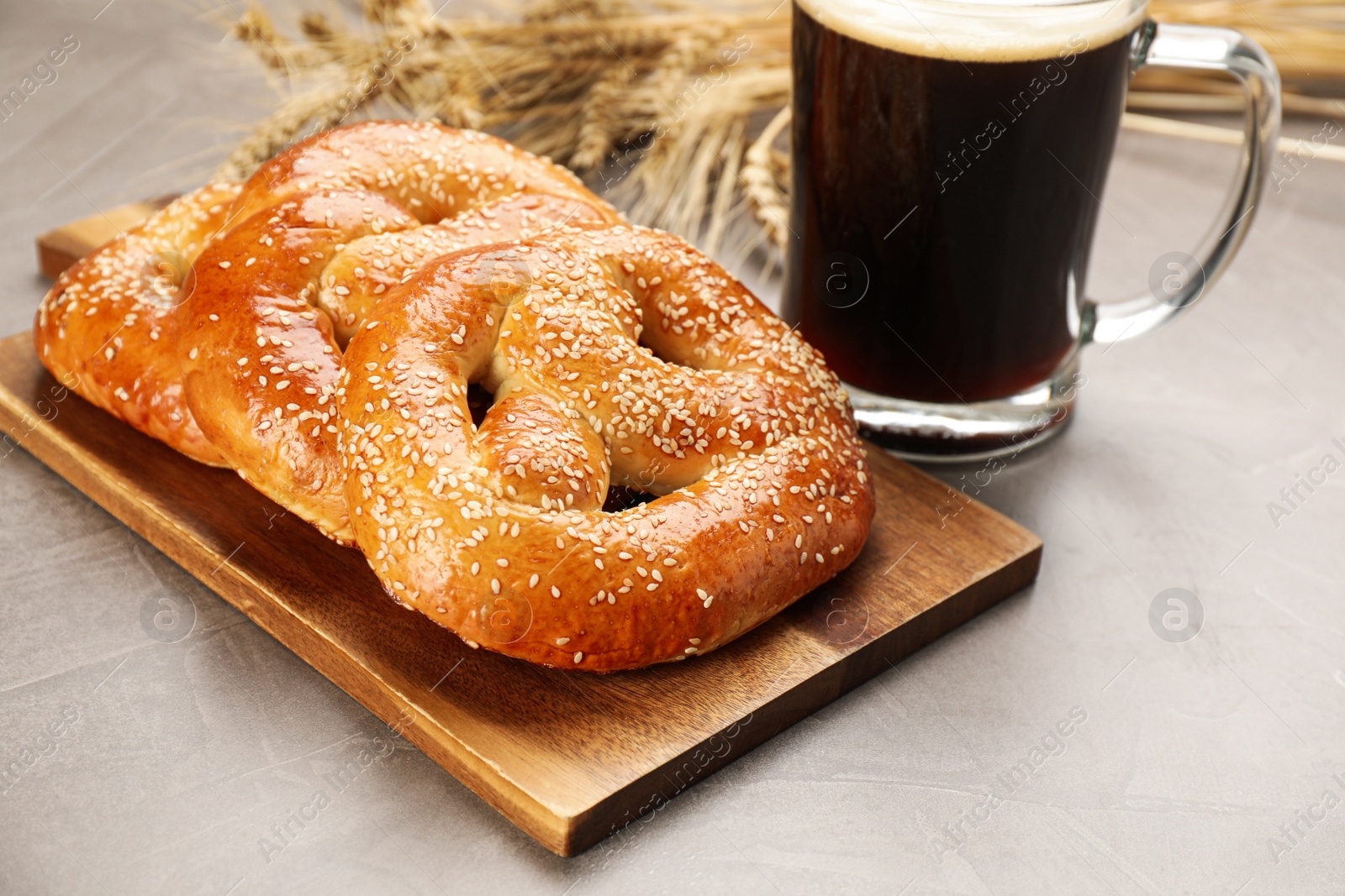 Photo of Tasty pretzels, glass of beer and wheat spikes on grey table