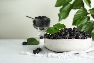 Bowl of delicious ripe black mulberries on white table, space for text