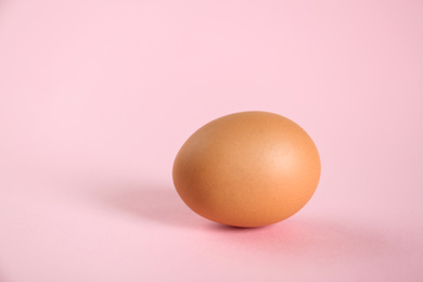 Raw brown chicken egg on pink background