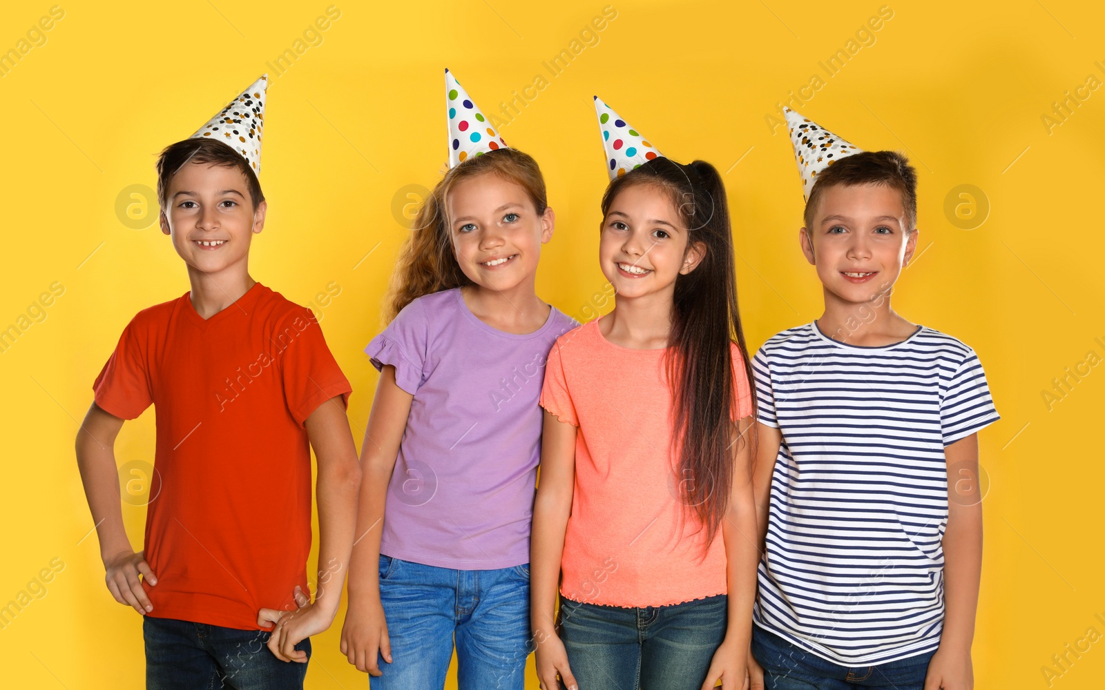 Photo of Happy children in party hats on yellow background. Birthday celebration