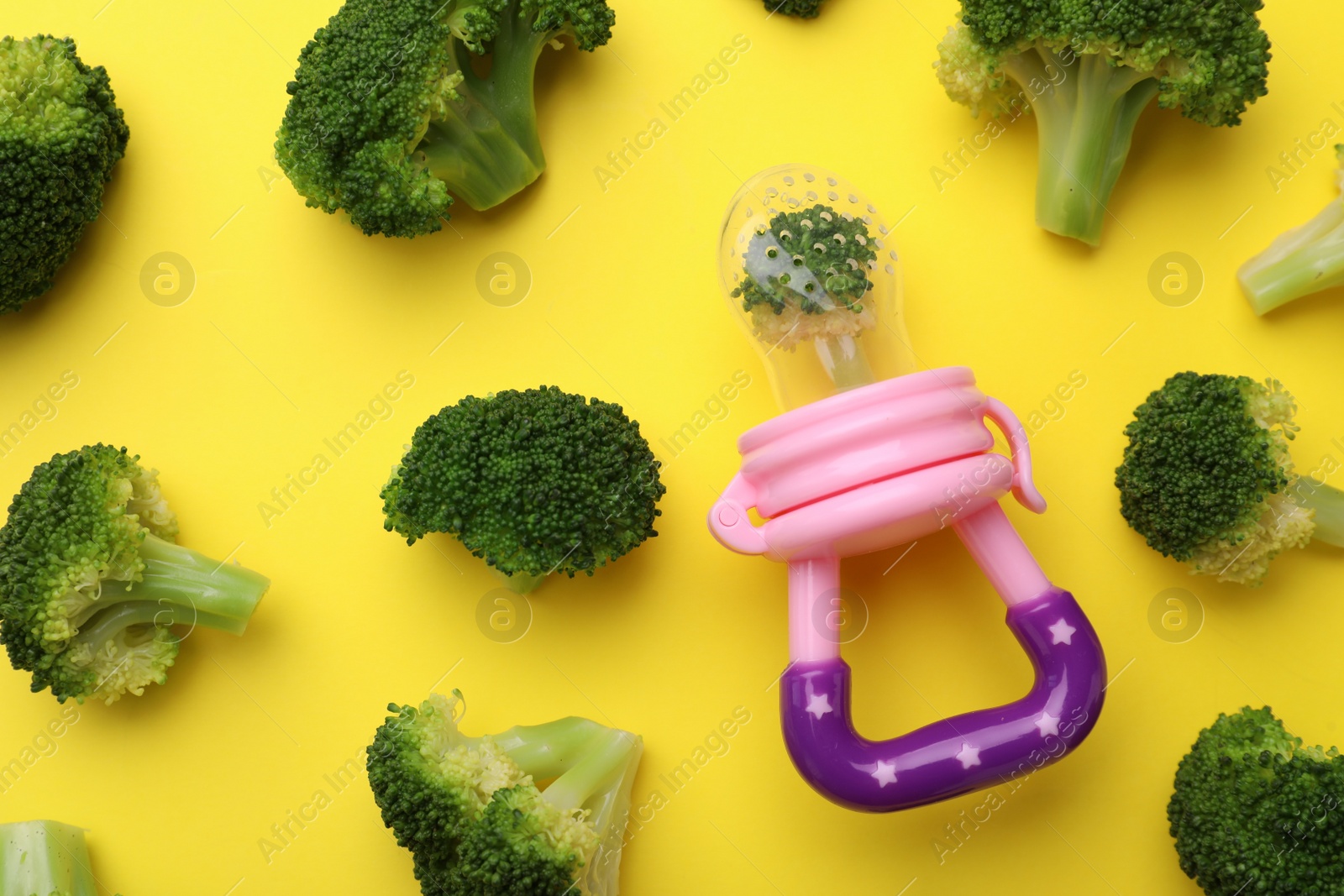 Photo of Nibbler with boiled broccoli on yellow background, flat lay. Baby feeder
