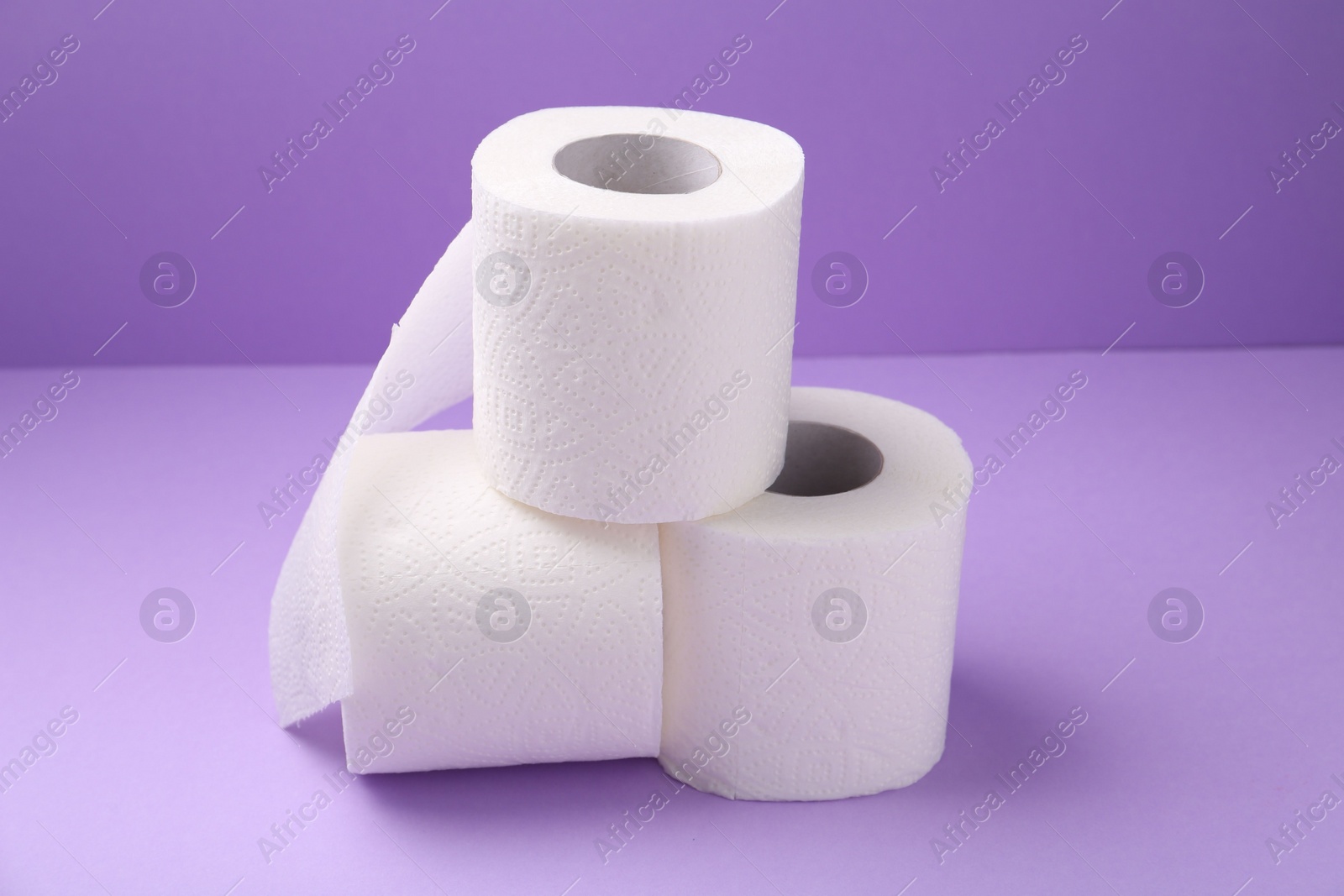 Photo of Soft toilet paper rolls on violet background, closeup