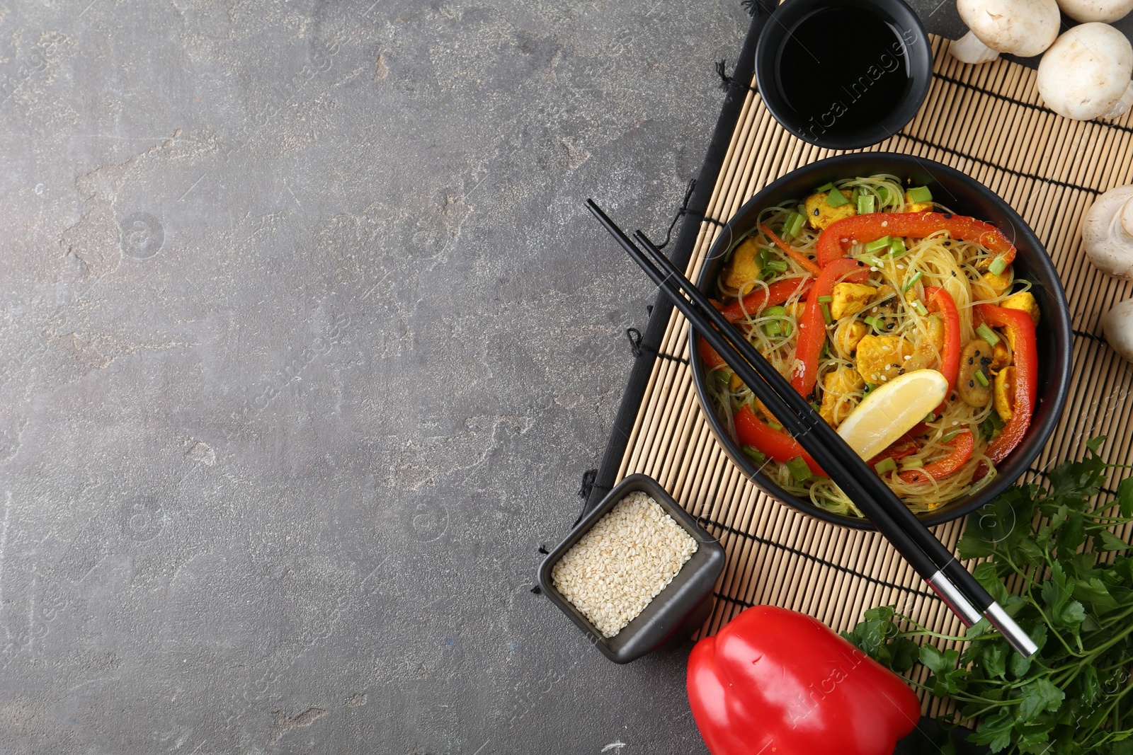 Photo of Stir-fry. Delicious cooked noodles with chicken and vegetables in bowl served on gray textured table, flat lay. Space for text