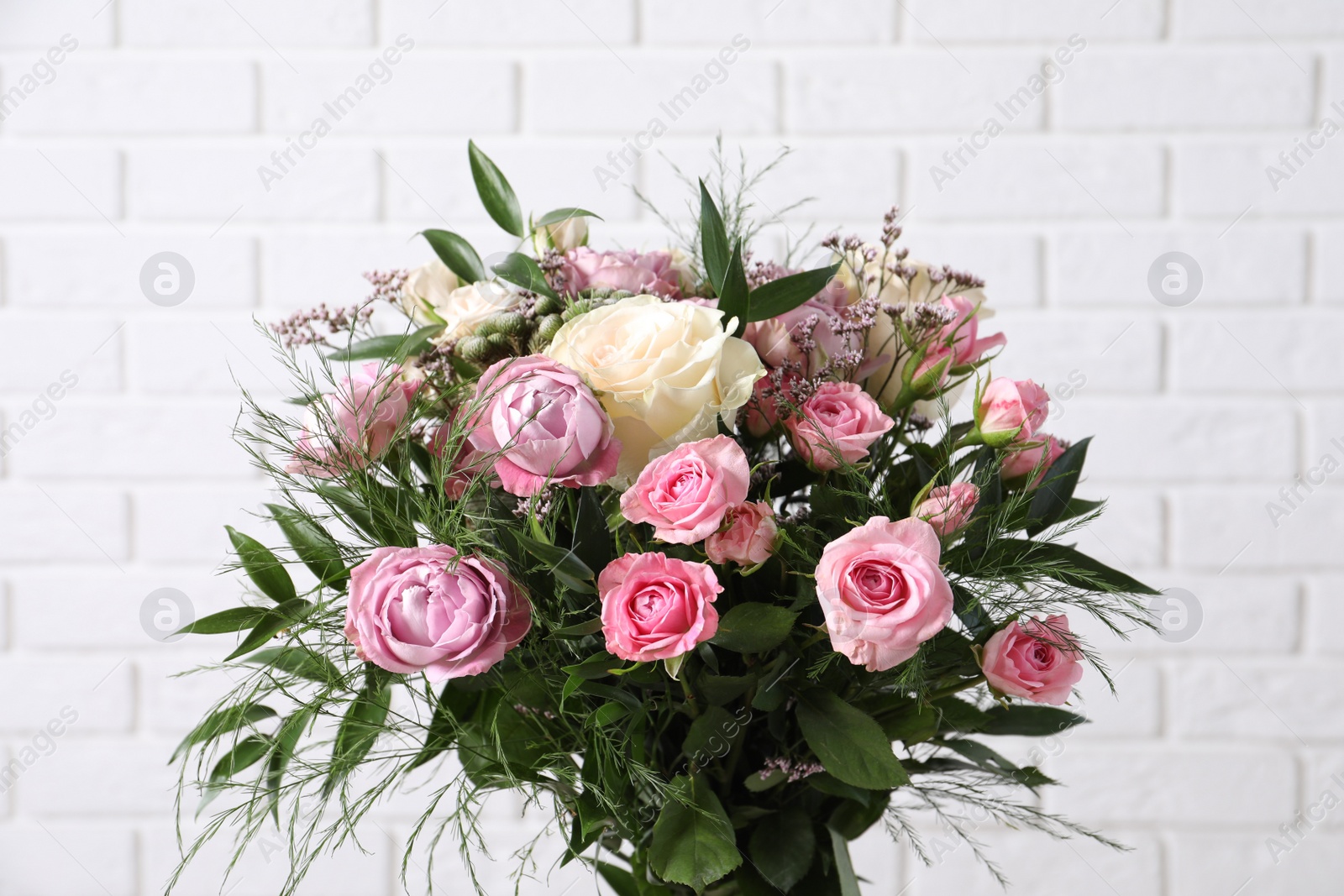 Photo of Beautiful bouquet with roses near white brick wall