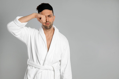 Photo of Sleepy young man in bathrobe on light grey background. Space for text